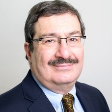 Professor of Decision Sciences and Statistics, Refik Soyer, wearing a blue suit with a yellow tie in front of a white background