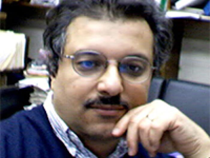 Professor of Statistics, Hosam M. Mahmoud, wearing a blue sweater in front of a bookshelf with his hand on his chin