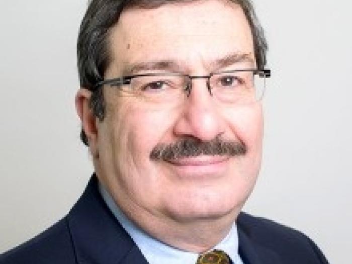 Professor of Decision Sciences and Statistics, Refik Soyer, wearing a blue suit with a yellow tie in front of a white background