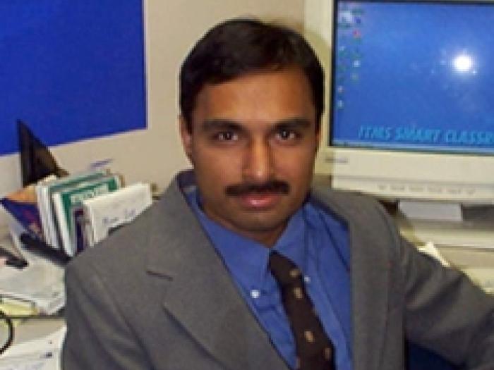 Undergraduate Program Director, Srinivasan Balaji, sitting at his desk in a grey suit and blue shirt