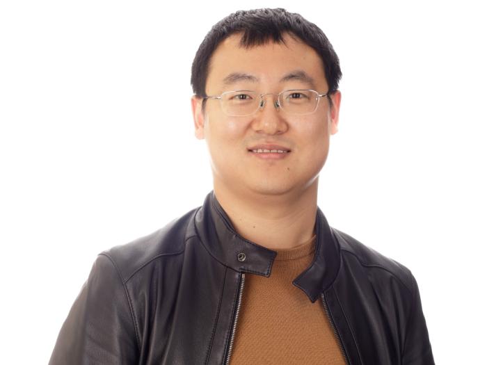 Assistant Professor, Xiaoke Zhang, wearing a leather jacket and yellow sweater in front of a white background