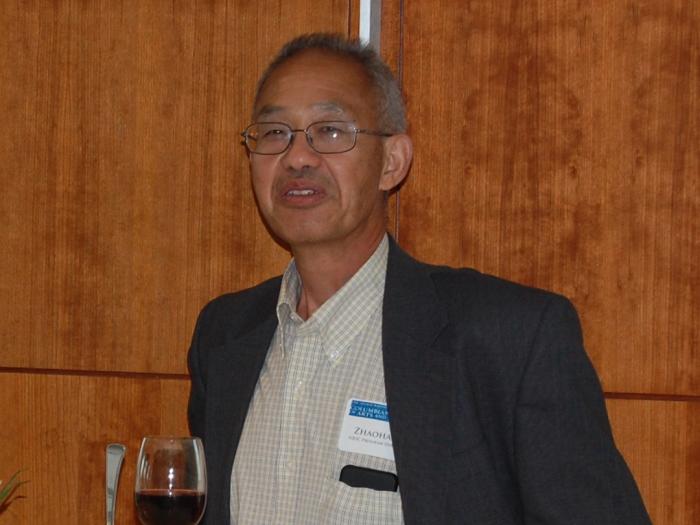 Professor of Statistics, Zhaohai Li, in a gray suit with a white shirt at a standing table